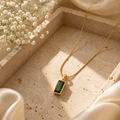 Gold necklace with a green pendant on a textured surface