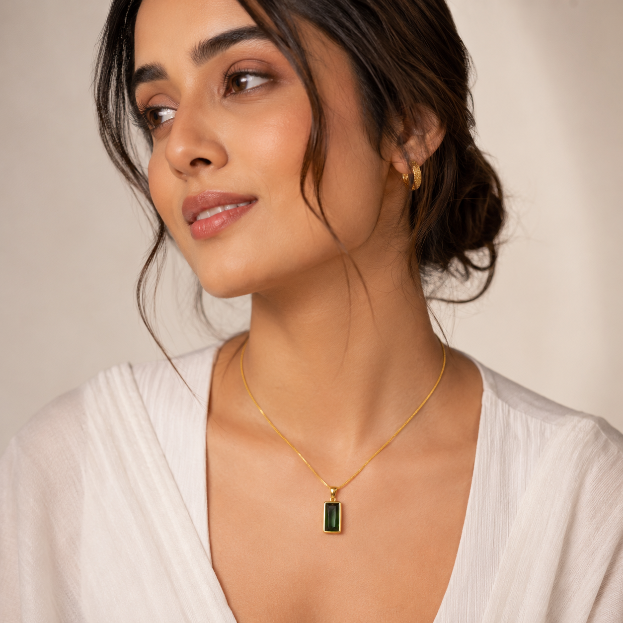 Model wearing a gold necklace with a green pendant